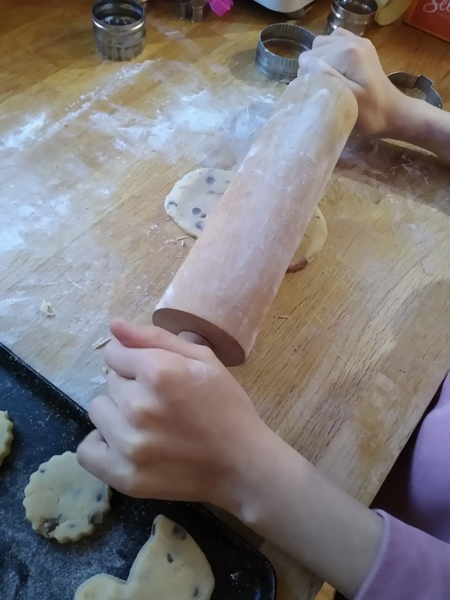 A child's hands rolling out shortbread dough on a floury worktop with cookie cutters